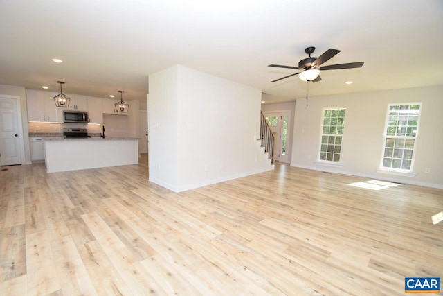 unfurnished living room featuring light wood-type flooring and ceiling fan with notable chandelier