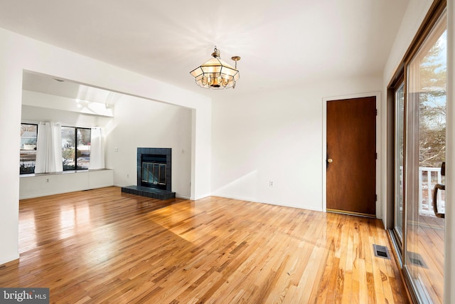 unfurnished living room featuring a tile fireplace, a chandelier, and light wood-type flooring