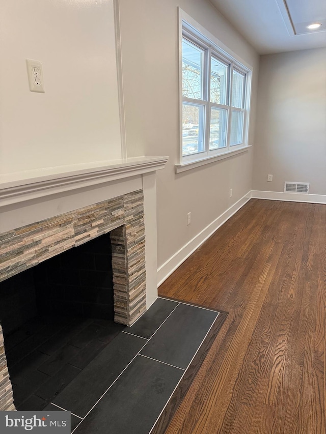 unfurnished living room featuring a stone fireplace and dark hardwood / wood-style floors