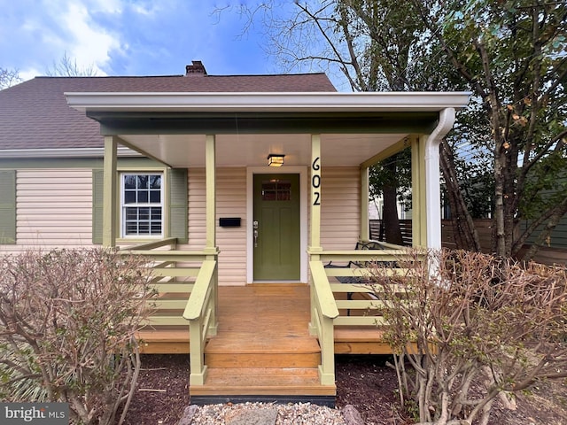 doorway to property with a porch, roof with shingles, and a chimney