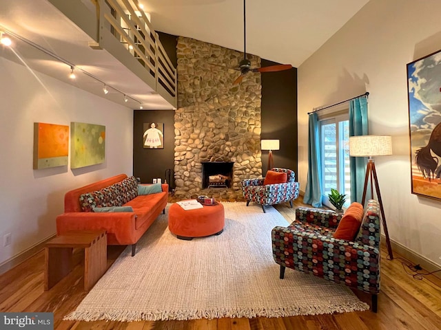 living area featuring baseboards, ceiling fan, wood finished floors, a stone fireplace, and high vaulted ceiling