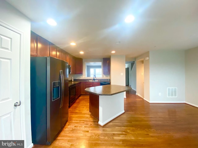 kitchen with sink, light hardwood / wood-style flooring, stainless steel fridge, black dishwasher, and a kitchen island