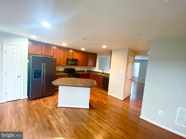 kitchen with light hardwood / wood-style floors, sink, black appliances, and a center island