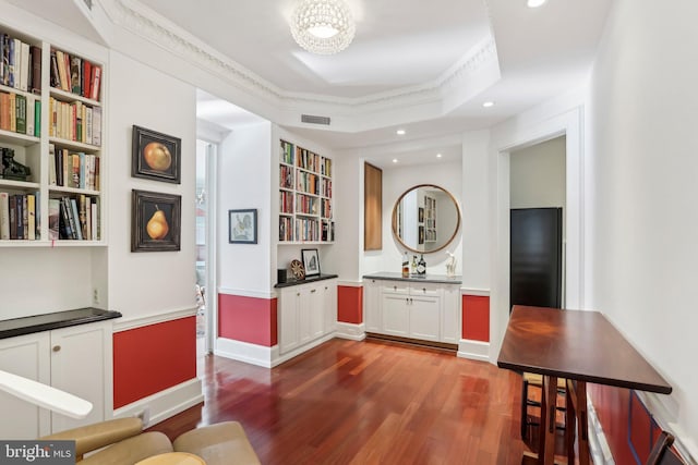 interior space featuring hardwood / wood-style floors, built in shelves, a raised ceiling, and ornamental molding