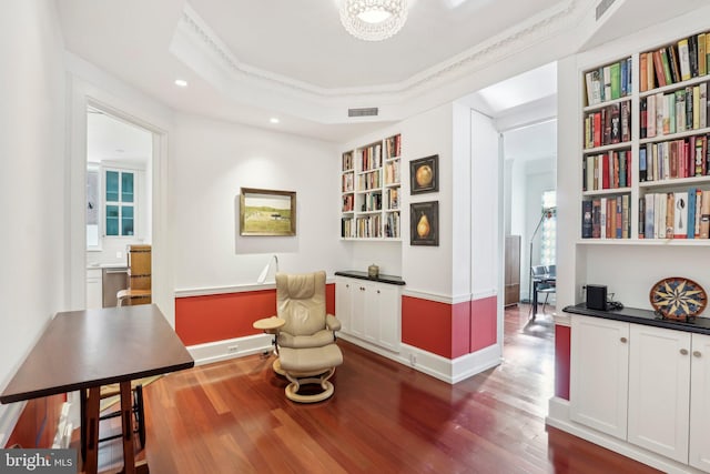 living area with dark hardwood / wood-style flooring, a raised ceiling, and ornamental molding