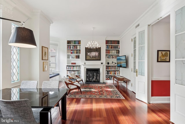 living room with built in features, ornamental molding, an inviting chandelier, and hardwood / wood-style floors