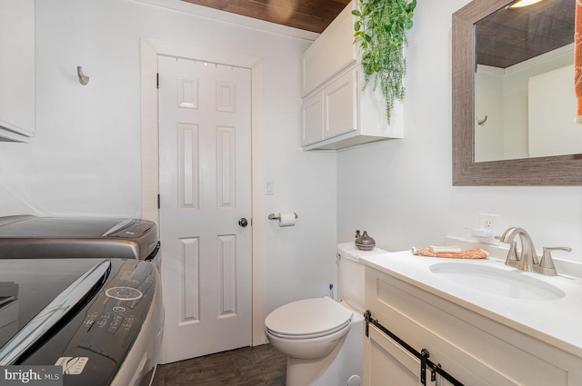 half bathroom with washing machine and dryer, vanity, toilet, and wood finished floors