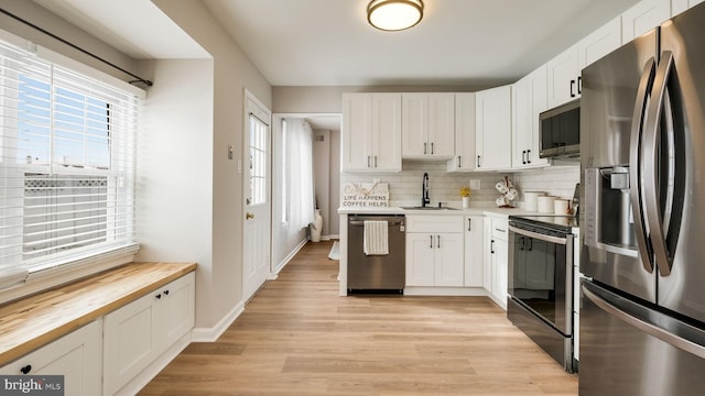 kitchen with appliances with stainless steel finishes, sink, backsplash, white cabinetry, and butcher block countertops