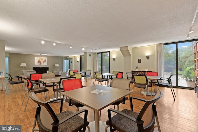 dining room with a wall of windows, light wood-style floors, a textured ceiling, and track lighting