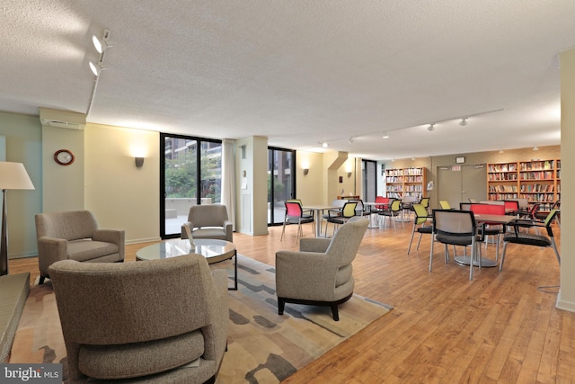 living room featuring expansive windows, a textured ceiling, track lighting, light wood-type flooring, and a wall mounted air conditioner