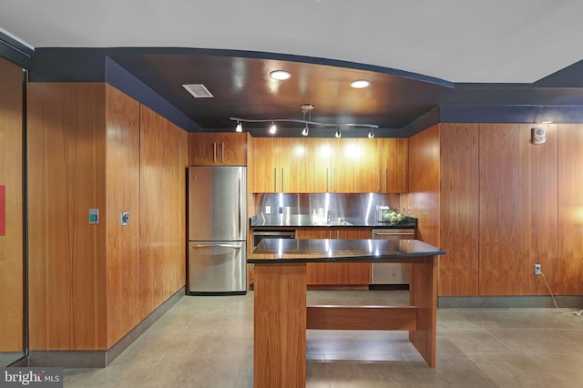 kitchen with rail lighting, appliances with stainless steel finishes, sink, and wooden walls