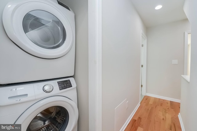 washroom with light hardwood / wood-style flooring and stacked washing maching and dryer