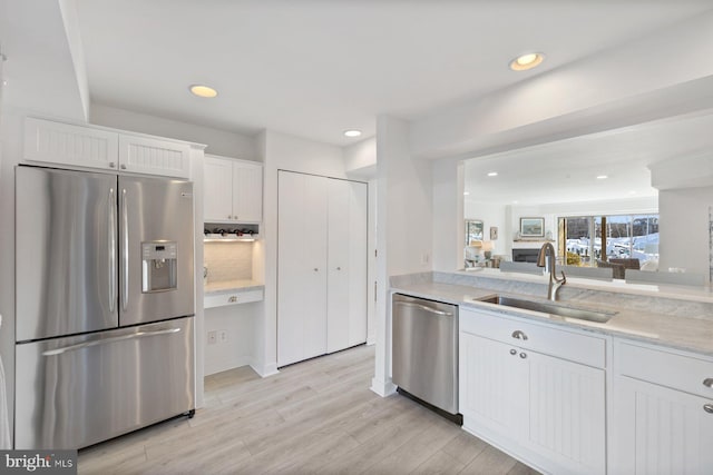 kitchen featuring sink, white cabinets, stainless steel appliances, light stone countertops, and light wood-type flooring