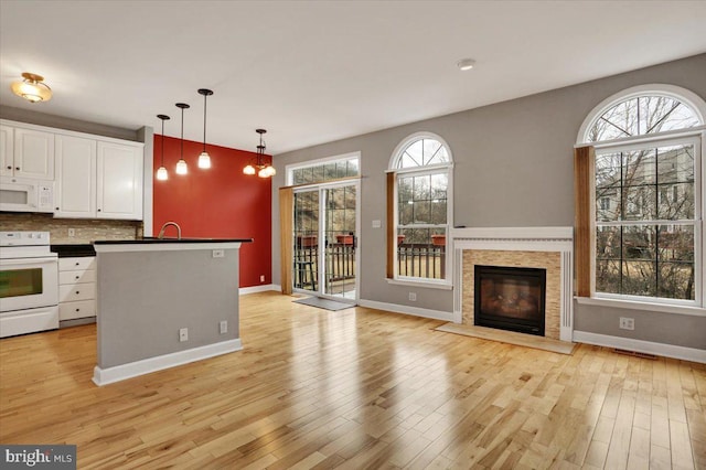 kitchen with dark countertops, hanging light fixtures, a fireplace with flush hearth, white cabinets, and white appliances