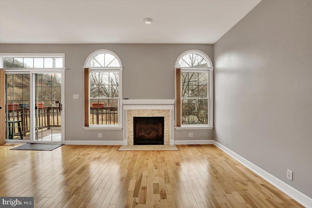 unfurnished living room with baseboards, a fireplace with flush hearth, and light wood-style floors