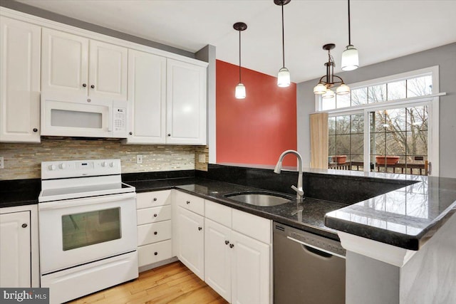 kitchen featuring a peninsula, white appliances, a sink, white cabinetry, and decorative light fixtures