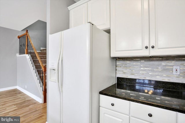 kitchen with white refrigerator with ice dispenser, white cabinetry, dark stone counters, and backsplash