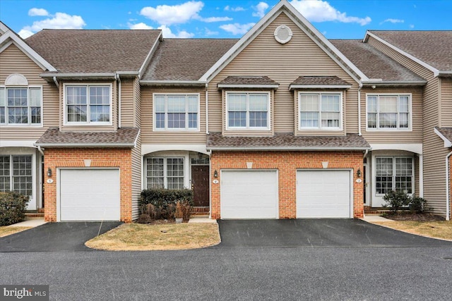 view of property with driveway, an attached garage, roof with shingles, and brick siding