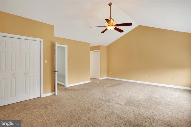 unfurnished bedroom with ceiling fan, carpet flooring, baseboards, vaulted ceiling, and two closets