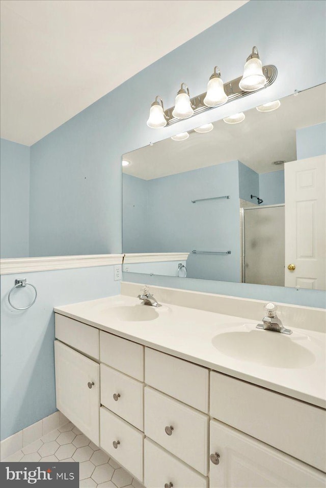 full bath featuring a stall shower, double vanity, a sink, and tile patterned floors