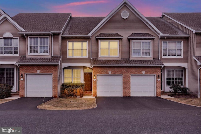 view of property with a garage, driveway, brick siding, and roof with shingles