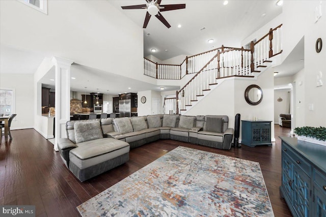 living room featuring dark wood-type flooring, ceiling fan, a towering ceiling, and ornate columns