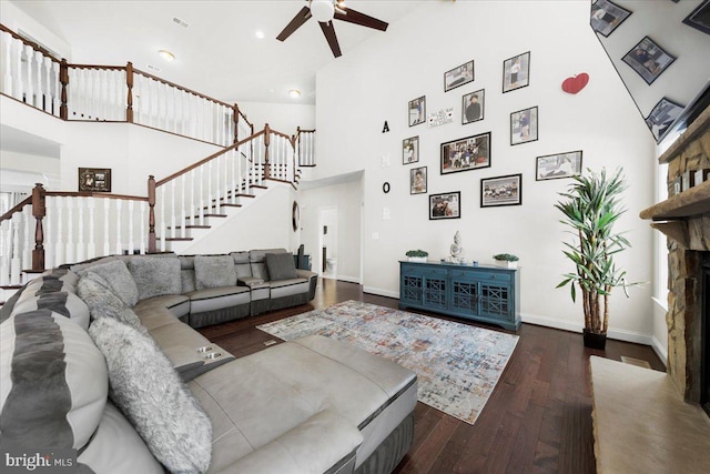 living room with dark hardwood / wood-style flooring, a fireplace, ceiling fan, and a high ceiling