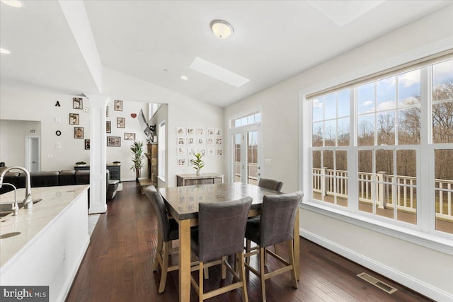 dining room with vaulted ceiling with skylight, dark hardwood / wood-style flooring, and ornate columns