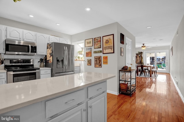 kitchen featuring ceiling fan, backsplash, stainless steel appliances, light hardwood / wood-style floors, and white cabinets