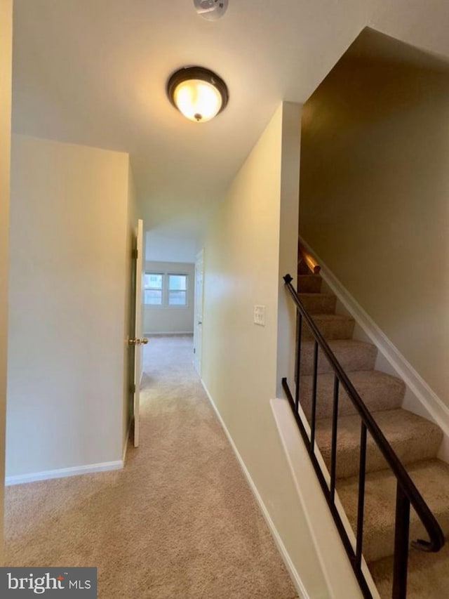 hallway featuring light carpet, baseboards, and stairs