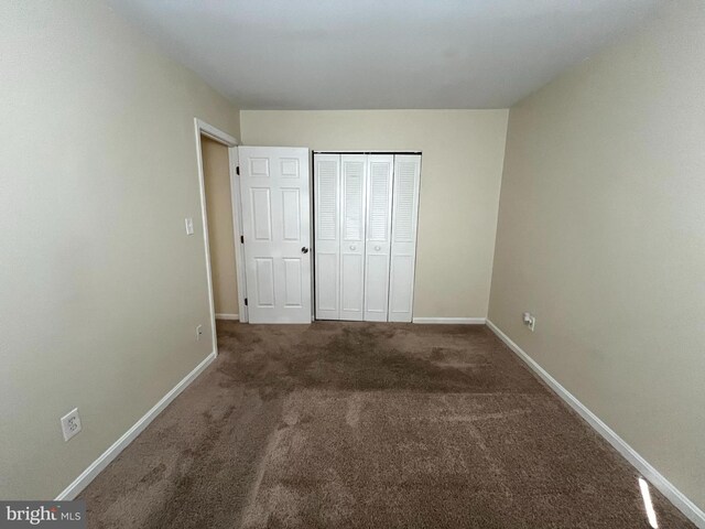 unfurnished bedroom with baseboards, dark carpet, and a closet