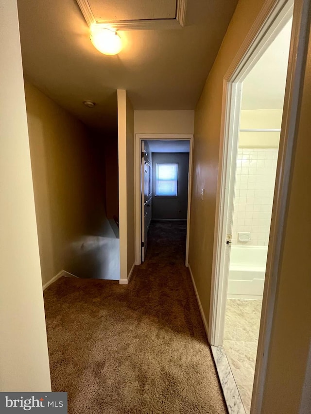 hallway featuring baseboards and dark carpet