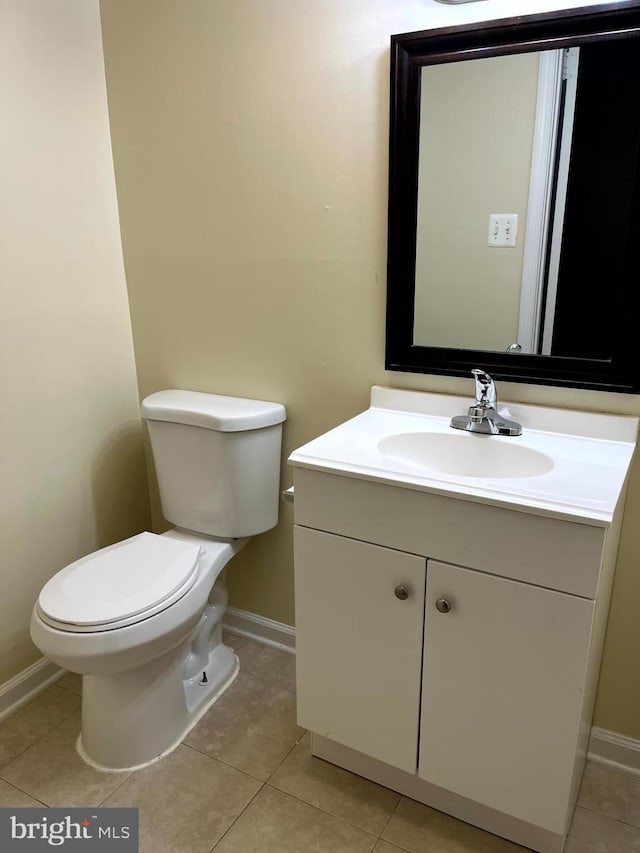 half bath with toilet, vanity, baseboards, and tile patterned floors