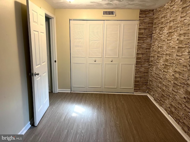 unfurnished bedroom featuring dark wood-style floors, a closet, visible vents, and baseboards