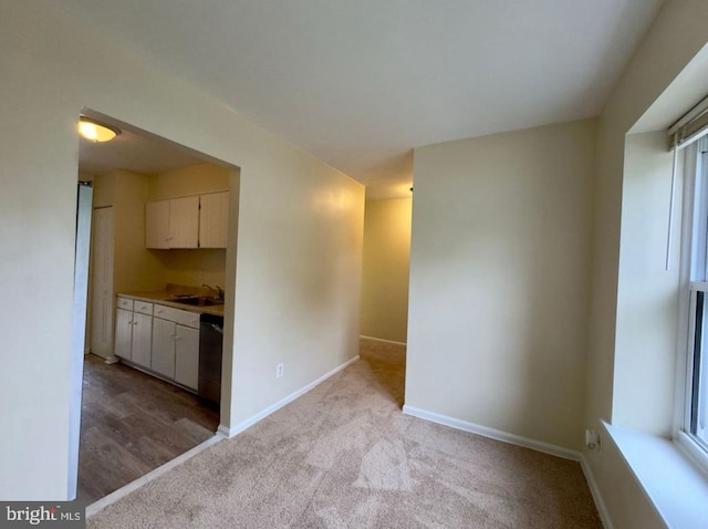 interior space featuring black dishwasher, sink, light carpet, and white cabinets