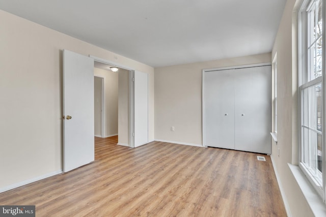 unfurnished bedroom with a closet, multiple windows, and light wood-type flooring