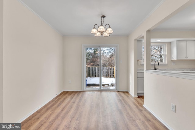 unfurnished dining area featuring a notable chandelier, sink, ornamental molding, and light hardwood / wood-style floors