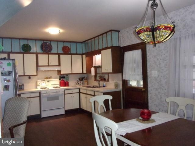 kitchen with white gas range oven, stainless steel refrigerator, white cabinets, and sink