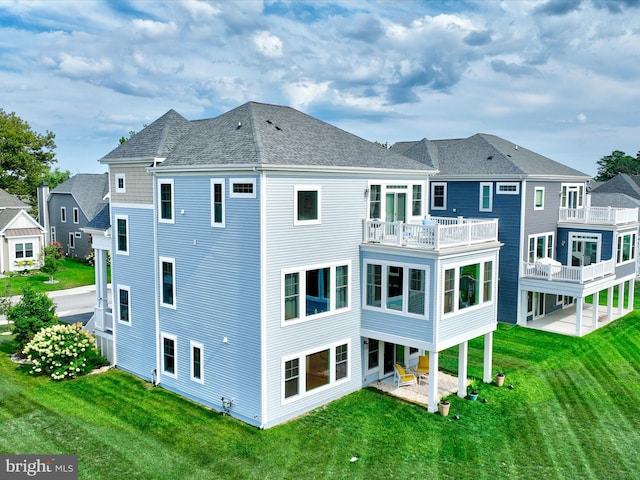 rear view of property with a balcony, a lawn, and a patio