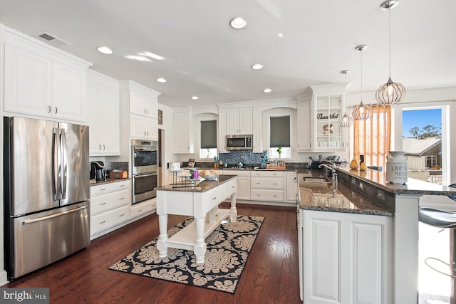 kitchen featuring white cabinets, appliances with stainless steel finishes, a center island, decorative light fixtures, and sink