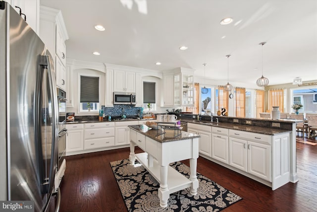 kitchen featuring white cabinets, a center island, decorative light fixtures, stainless steel appliances, and dark stone countertops