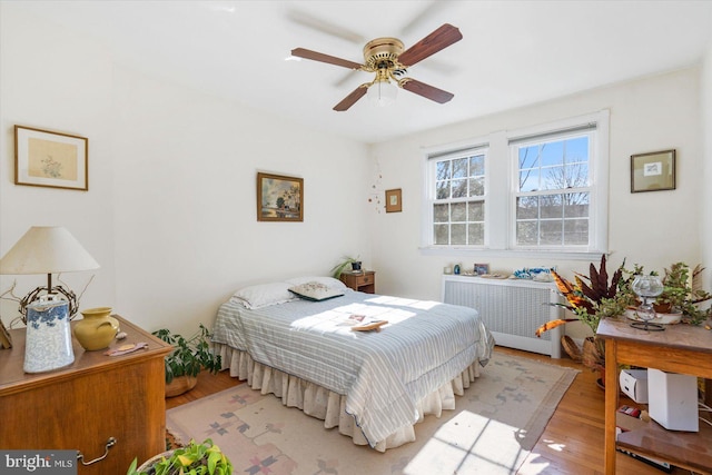 bedroom with ceiling fan, radiator heating unit, and light hardwood / wood-style floors