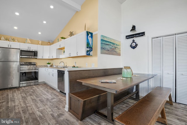 kitchen featuring hardwood / wood-style flooring, appliances with stainless steel finishes, white cabinets, and high vaulted ceiling