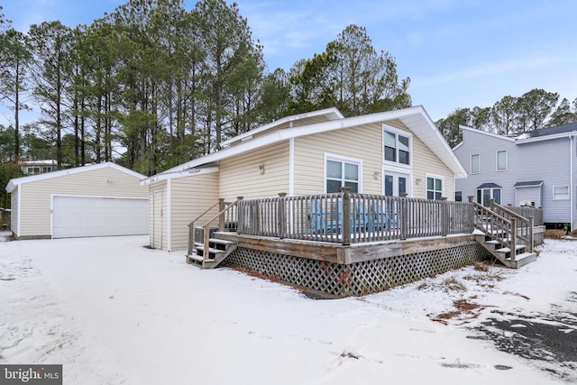 snow covered property featuring a garage, an outbuilding, and a deck