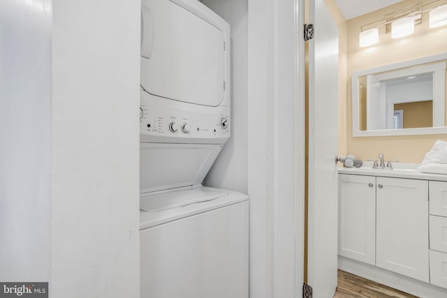 laundry room with sink, hardwood / wood-style flooring, and stacked washing maching and dryer