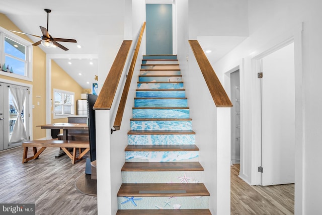 stairway with ceiling fan, wood-type flooring, and high vaulted ceiling