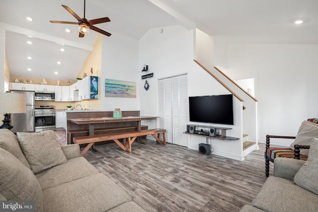 living room with ceiling fan, high vaulted ceiling, sink, and light hardwood / wood-style flooring