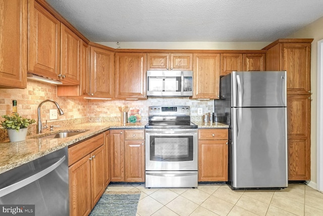 kitchen with light stone countertops, light tile patterned floors, decorative backsplash, sink, and stainless steel appliances