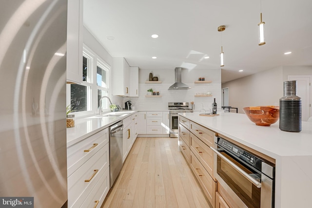 kitchen featuring white cabinetry, wall chimney range hood, decorative light fixtures, and appliances with stainless steel finishes