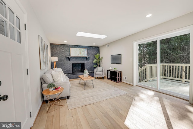 living room featuring a fireplace, a skylight, and light hardwood / wood-style floors